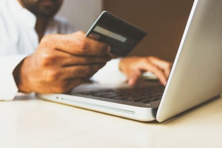 man holding credit card up beside computer